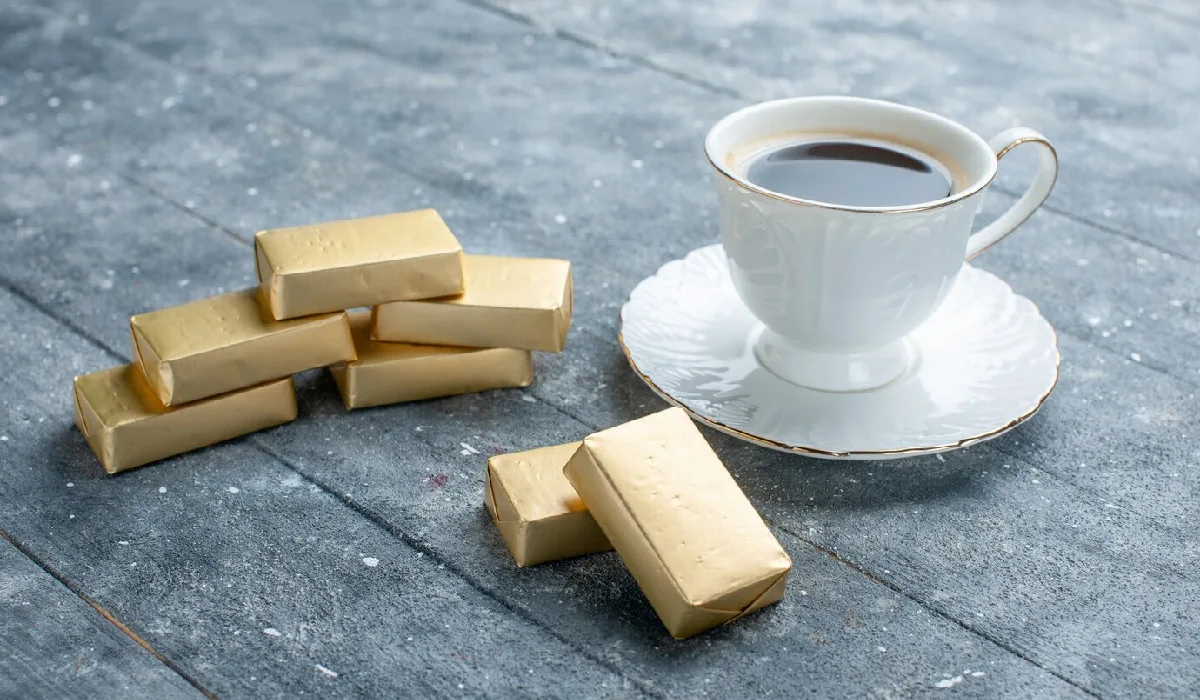 یک فنجان قهوه با قطعات کوچکی از شمش طلا در کنارش