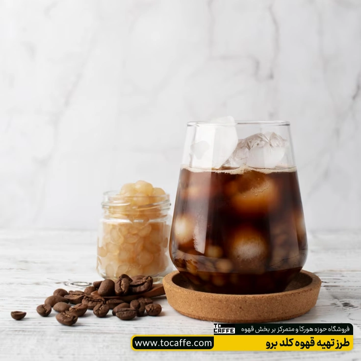 یک لیوان قهوه کلد برو که در کنار آن مقداری دان قهوه ریخته شده است.